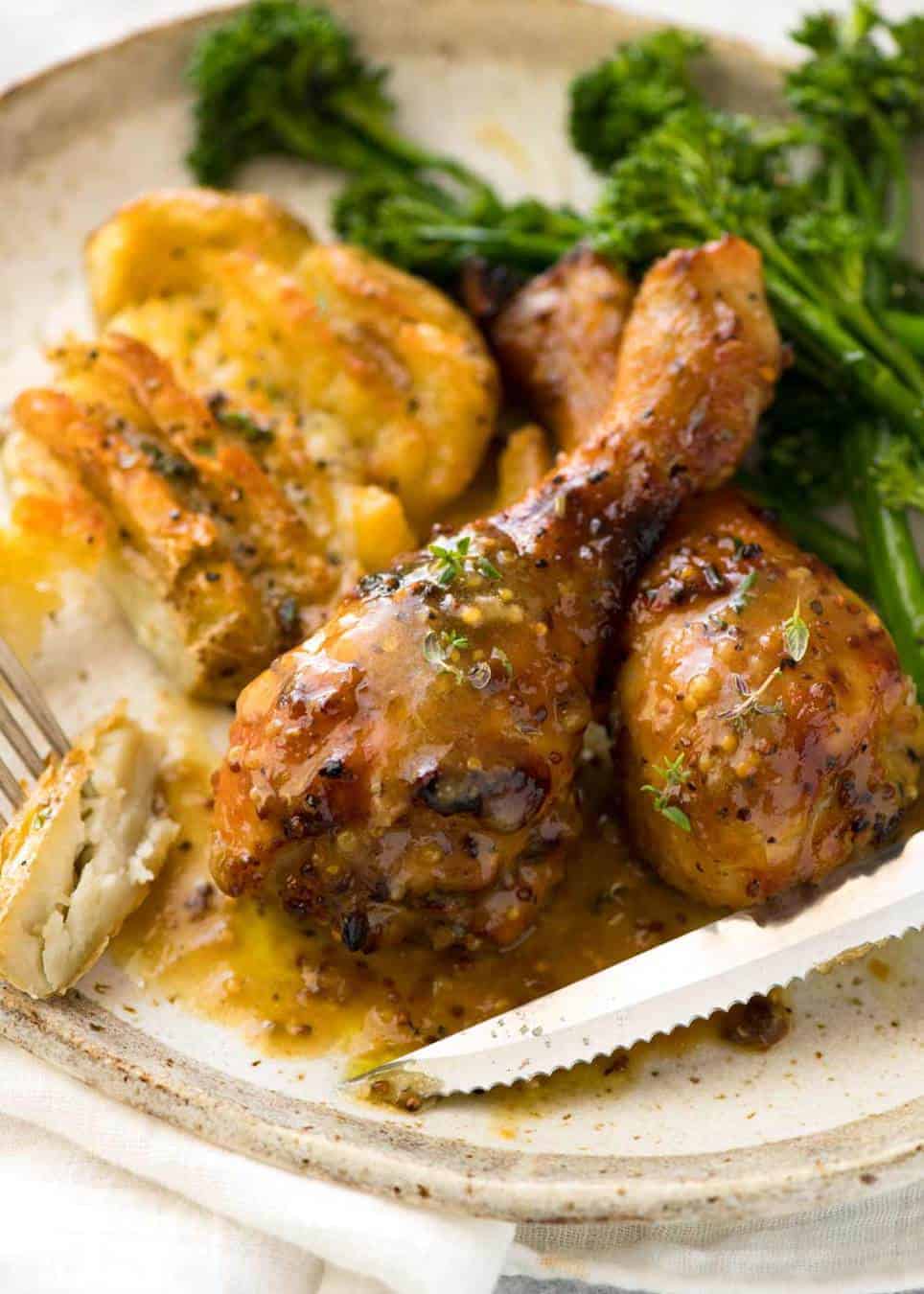 Honey Mustard Baked Chicken Drumsticks with Smashed Potatoes on a silver tray with a side of steamed broccolini on a rustic ceramic plate, ready to be eaten